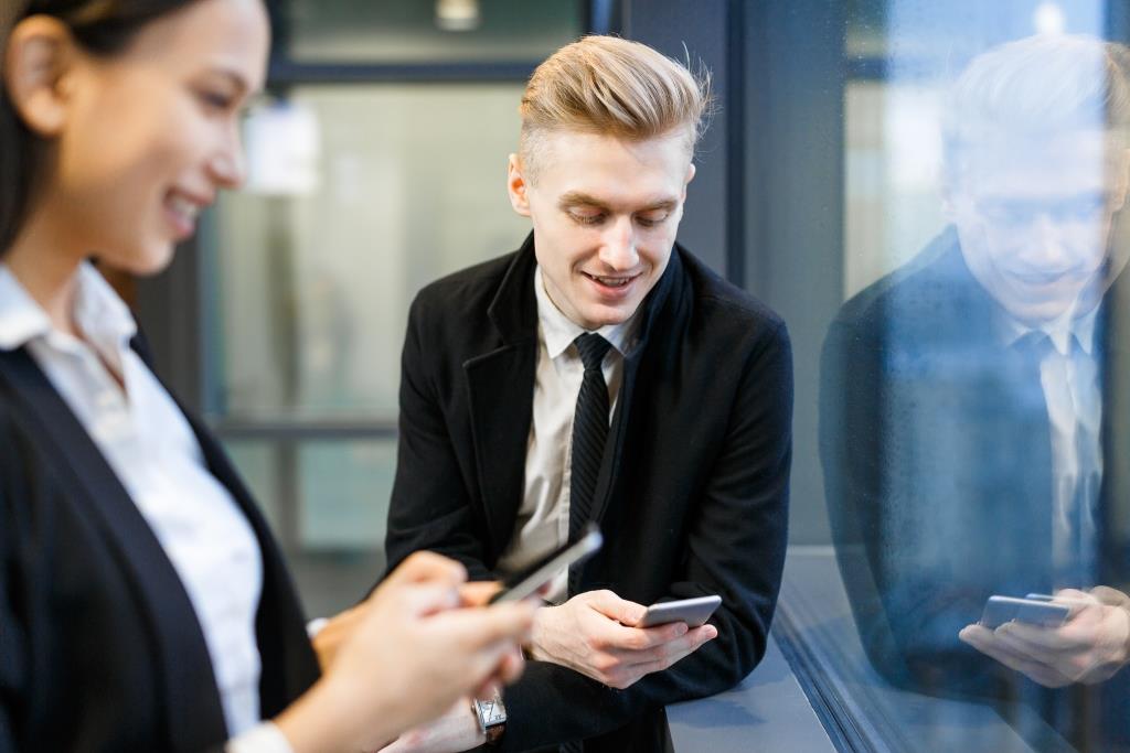 Contemporary office workers with cellphones standing by window